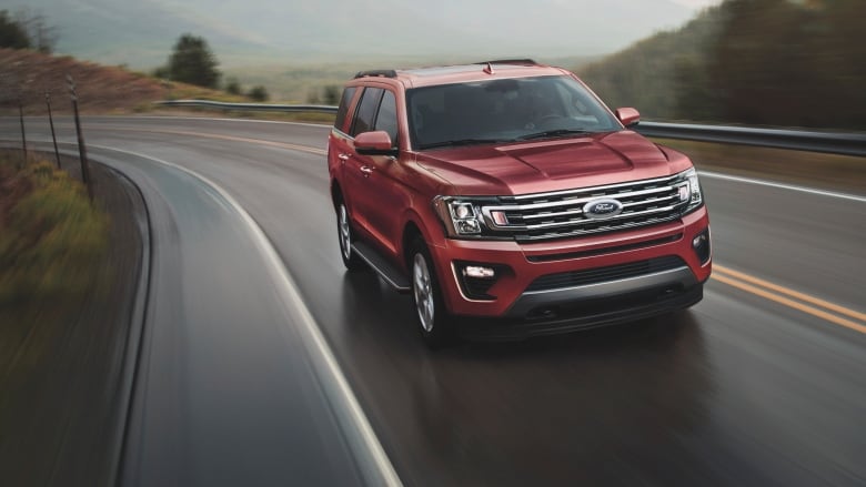 A red SUV drives down a highway with countryside in the background.