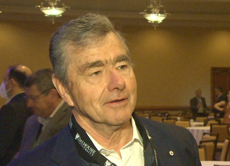 An older man wearing a suit stands in a hotel ballroom.