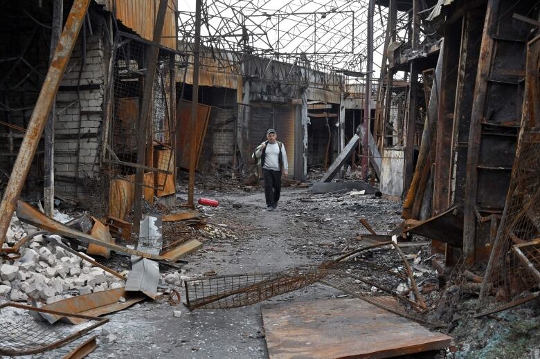 A man walks through a burned out market building in Kharkiv, Ukraine, that is littered with rubble and twisted metal.  