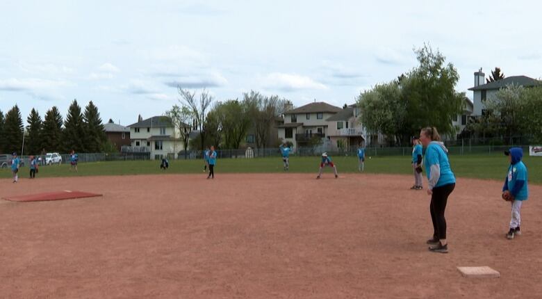 Girls and coaches in blue jersey stand in position on a baseball diamond in suburban Calgary. 