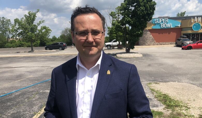 Irek Kusmierczyk stands in a parking lot wearing a white button up shirt and a blue blazer jacket smiling into the camera.