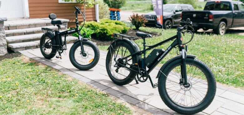 Two e-bikes sit parked in a driveway.