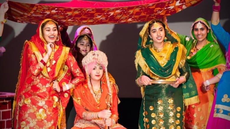 A group of young women dressed in colourful Punjabi clothing are dancing. 