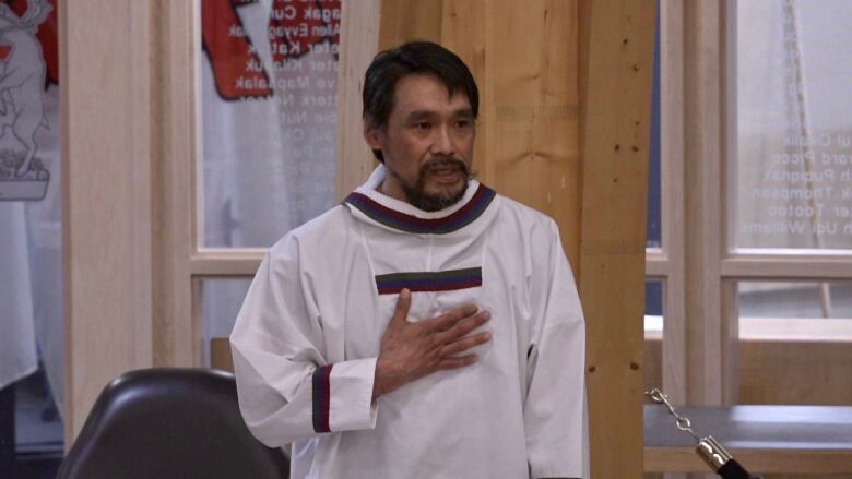 A man wearing a traditional Inuit shirt puts his right hand on his chest as he speaks to the legislative assembly. 