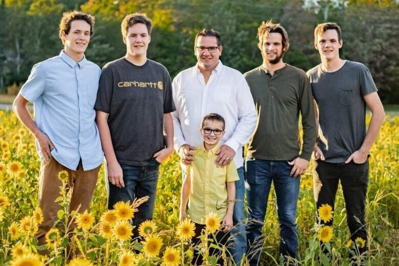 A family portrait of a dad and his five sons in a sunflower field.