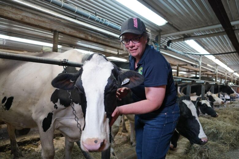 A woman stands in a barn, her arm draped over a dairy cow.