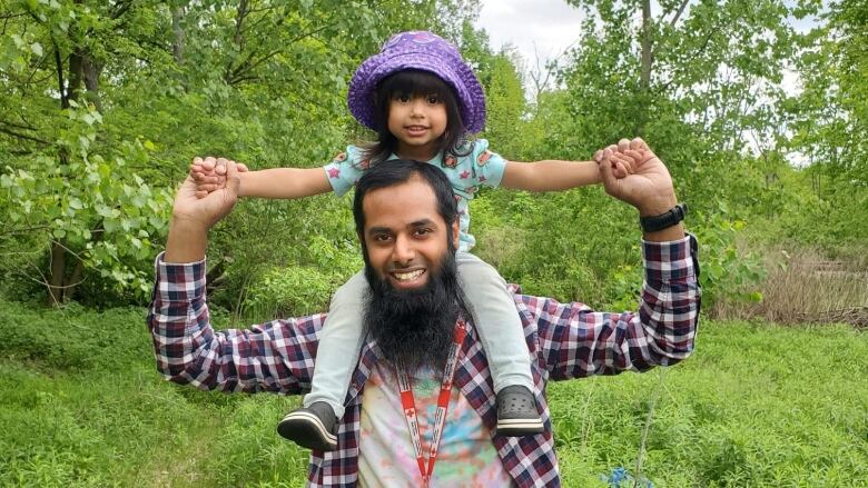 A dad carries his young daughter on his shoulders.