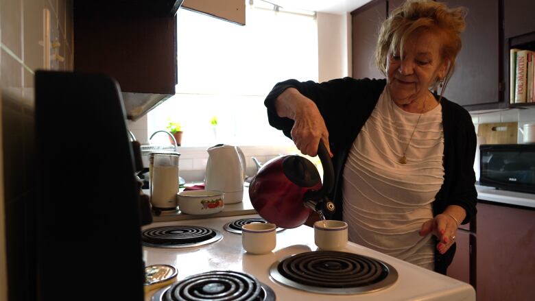 A woman pours herself a cup of tea in her kitchen.