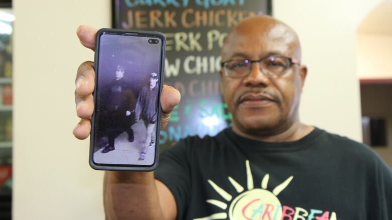 A picture of Michael Andrade holding up a phone with a picture of the two suspects.