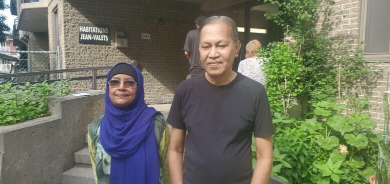 A couple stands outside an apartment block door.