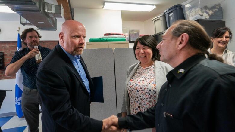 Two men shake hands, while others around them smile.