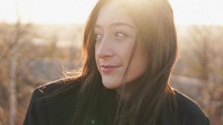 A woman looks off camera and wind is blowing in her long hair. she's outside but the background is blurry. 