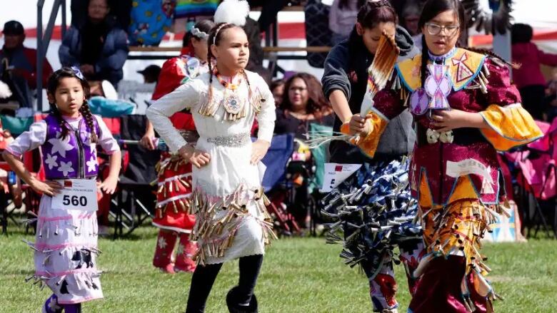 Indigenous youth dance in colourful jingle dresses at a powwow.