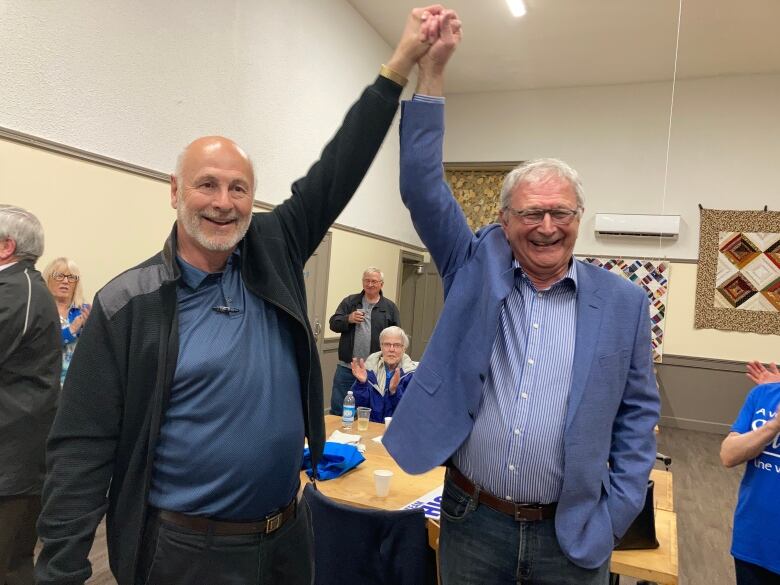 Two men hold hands, raising hands above their heads in victory signal.