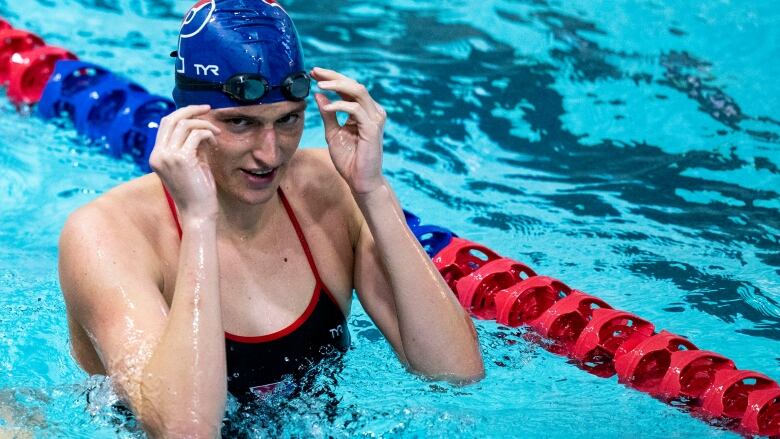 Female athlete adjusts her swim cap and goggles in pool.