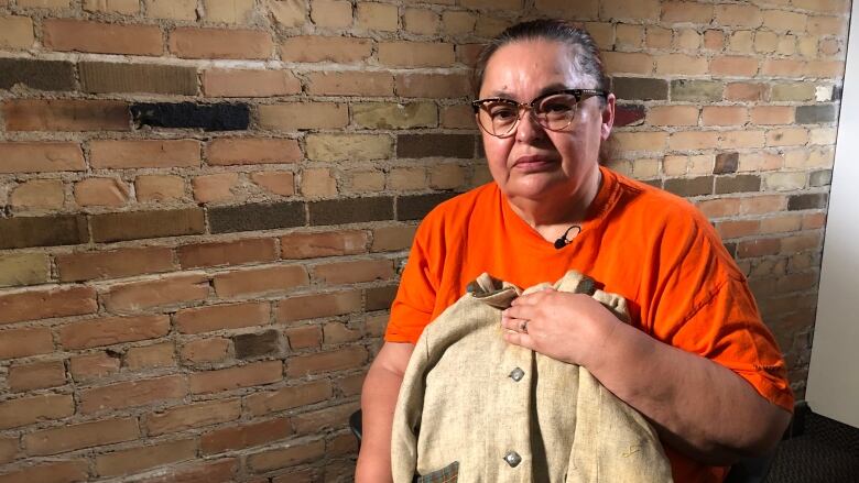 Woman in an orange shirt holds a child-sized beige jacket.