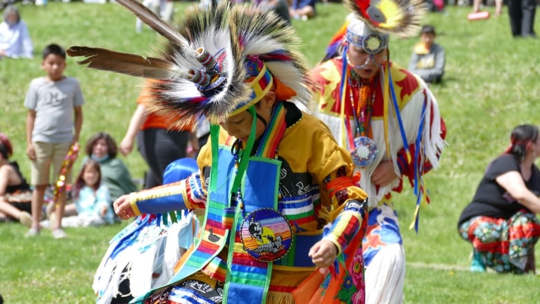 A boy dances in a field in a brightly-coloured Indigenous outfit.