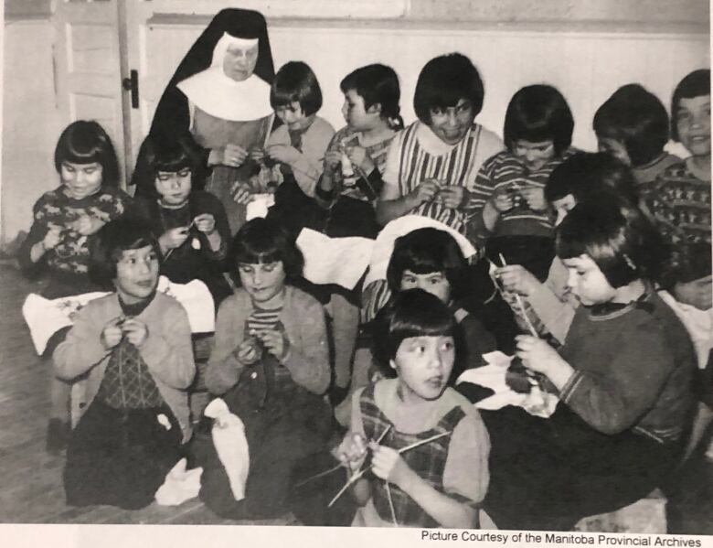 Black-and-white photo of over a dozen children and nun in a habit.