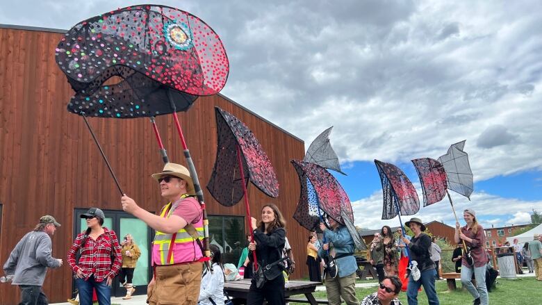 Smiling people walk in a line outdoors holding flags shaped like the various body parts of a salmon, for National Indigenous Peoples Day on June 21, 2022.