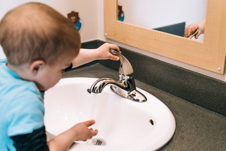 A child uses a bathroom tap with a copper handle.