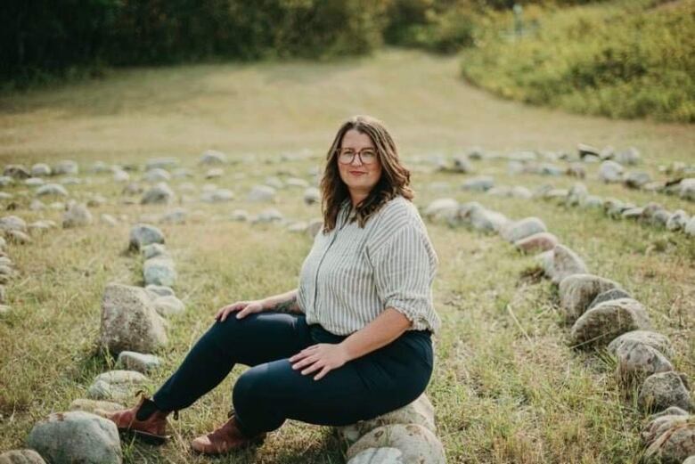 A woman sits on a rock in a field where they have been placed in concentric circles. 