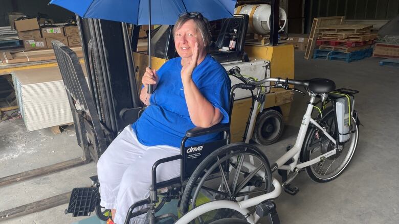 A woman sits in a wheelchair mounted on the front of an adapted bicycle.