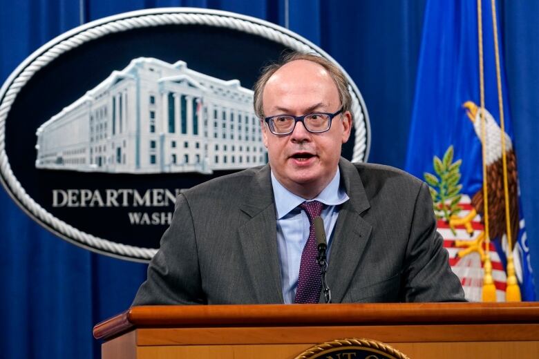 A man with glasses standing at a podium at the U.S. Justice Department.