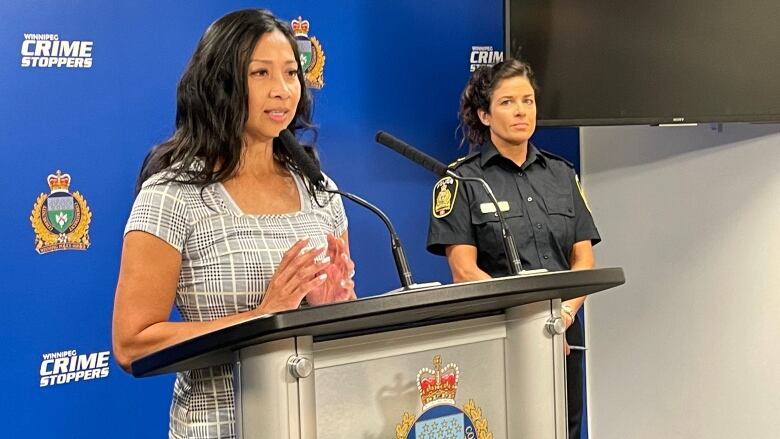 A woman speaks at a podium at Winnipeg police headquarters, with a police officer standing behind her. 