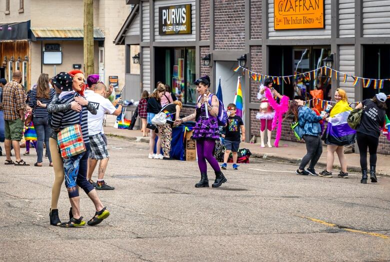 People are hugging and laughing on a street full of colourful flags and rainbow decorations.