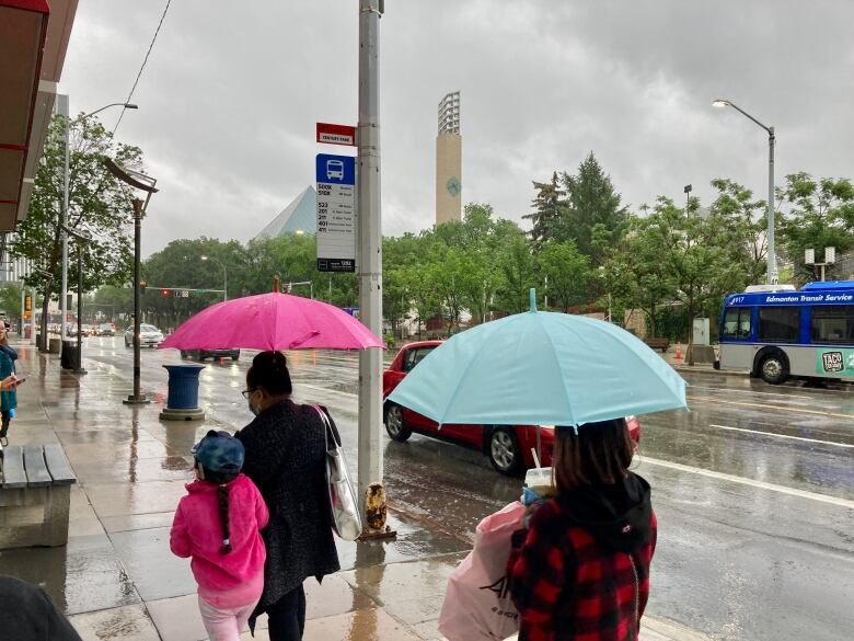 Two pedestrians with umbrellas walk down a wet city street.