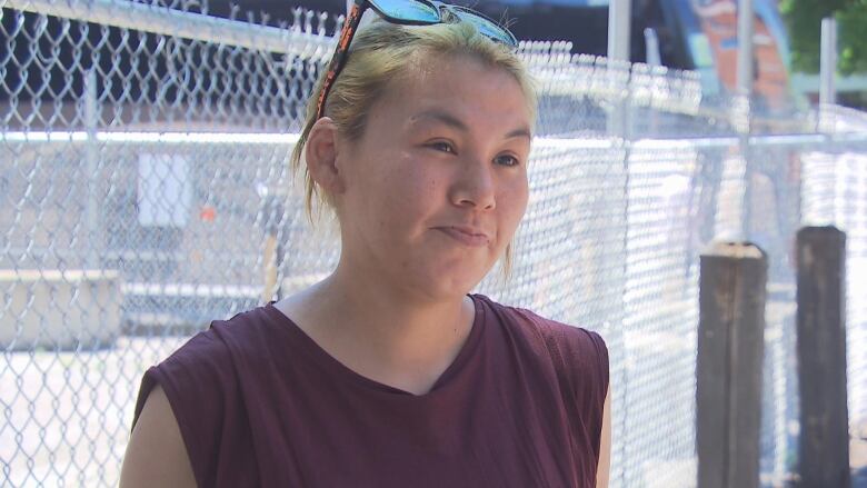 An Indigenous woman stands in front of fence enclosing an unused concrete lot. 