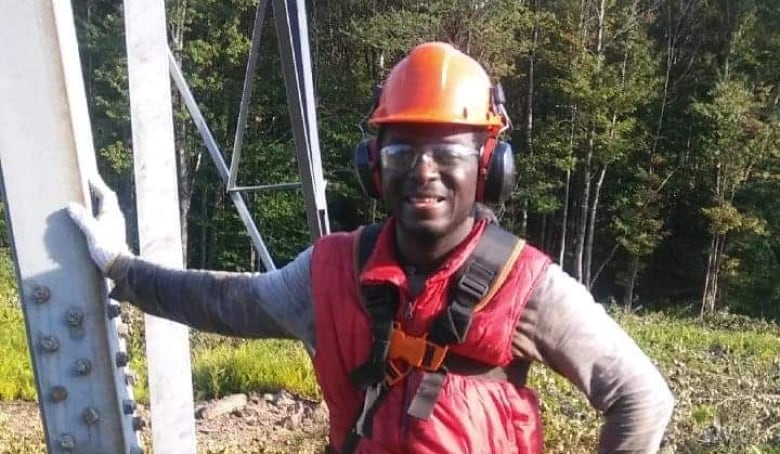 A man with an orange helmet leans on a hydro installation.