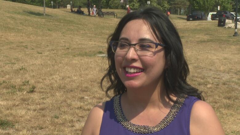 A smiling woman stands in a park. 