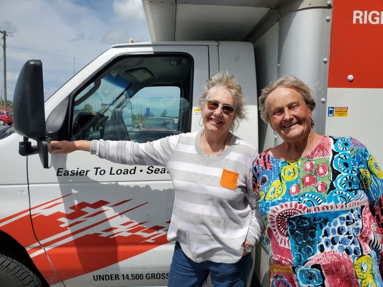 Two women stand in front of a U-Haul moving van.