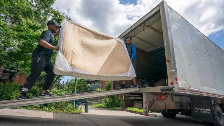 Two movers grasp a mattress as they place it into a storage truck. 