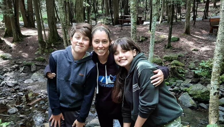 A woman standing with her two children in a forest.