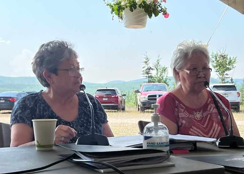 Two women participating in a meeting held outdoors in a tent.