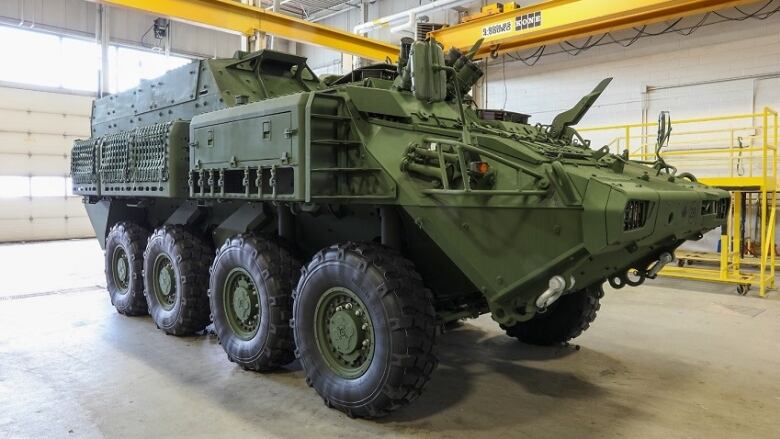 A large, green military vehicle with eight tires is parked inside a building near a large door.