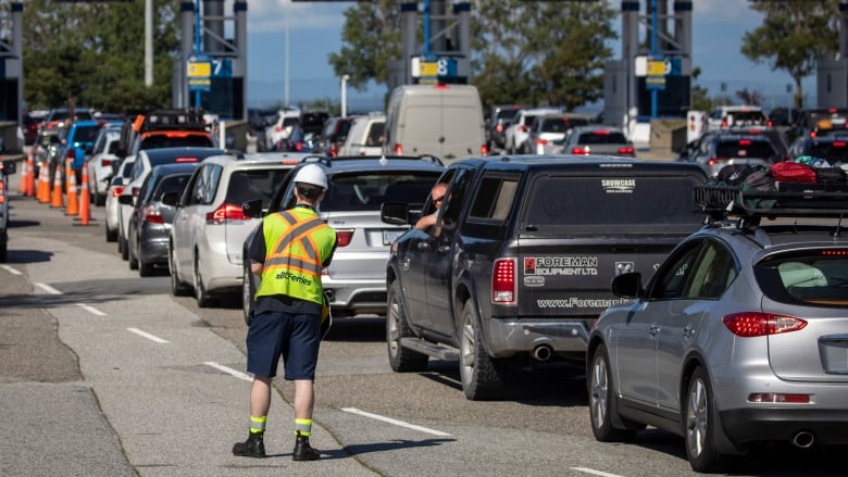 A person in a high-vis jacket stands on the road among dozens of lined-up cars.