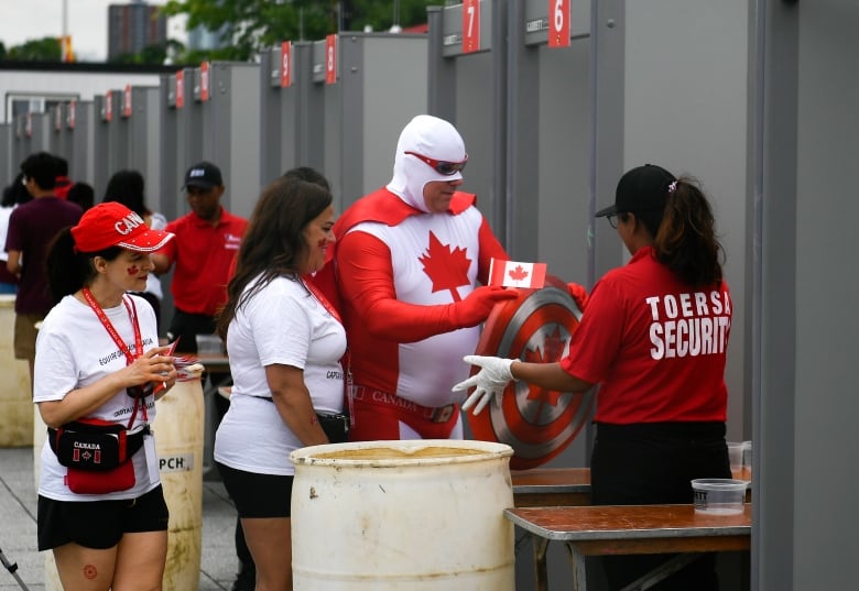 Several people, including a man in a costume, walk through a security checkpoint.