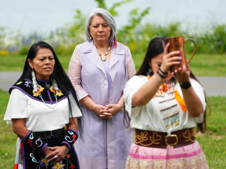 Three people stand together while taking part in a ceremony.