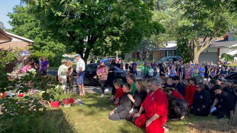 A crowd of people kneels outside a suburban home.