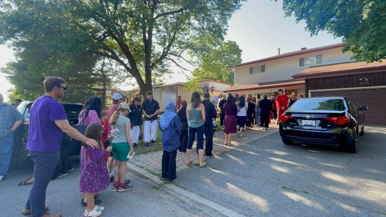 People stand in line outside a suburban home.