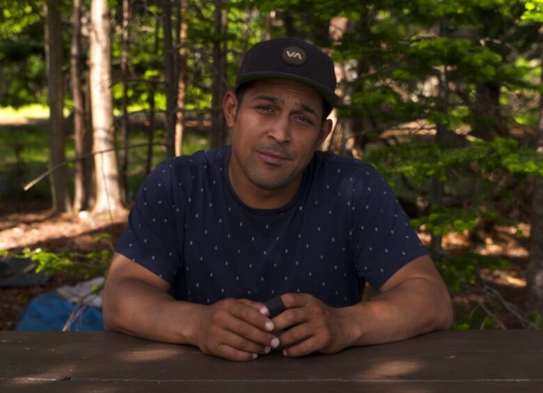 A man wearing a T-shirt and a baseball cap sits at a picnic table in Pippy Park. 