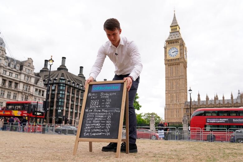 A man puts out a chalkboard in Parliament Square with the latest odds on when Johnson will resign and who will replace him in London, Wednesday July 6, 2022.