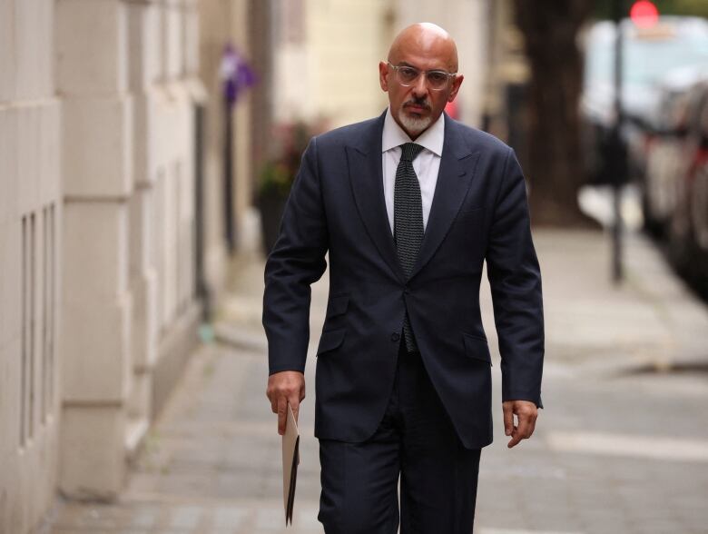 A bald man in a suit walks down a street. 