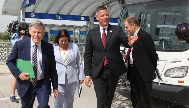 Four people stand in front of a bus at a transit stop.