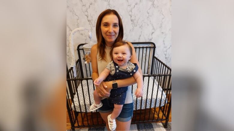 A woman holds her five-month-old son in front of his crib.