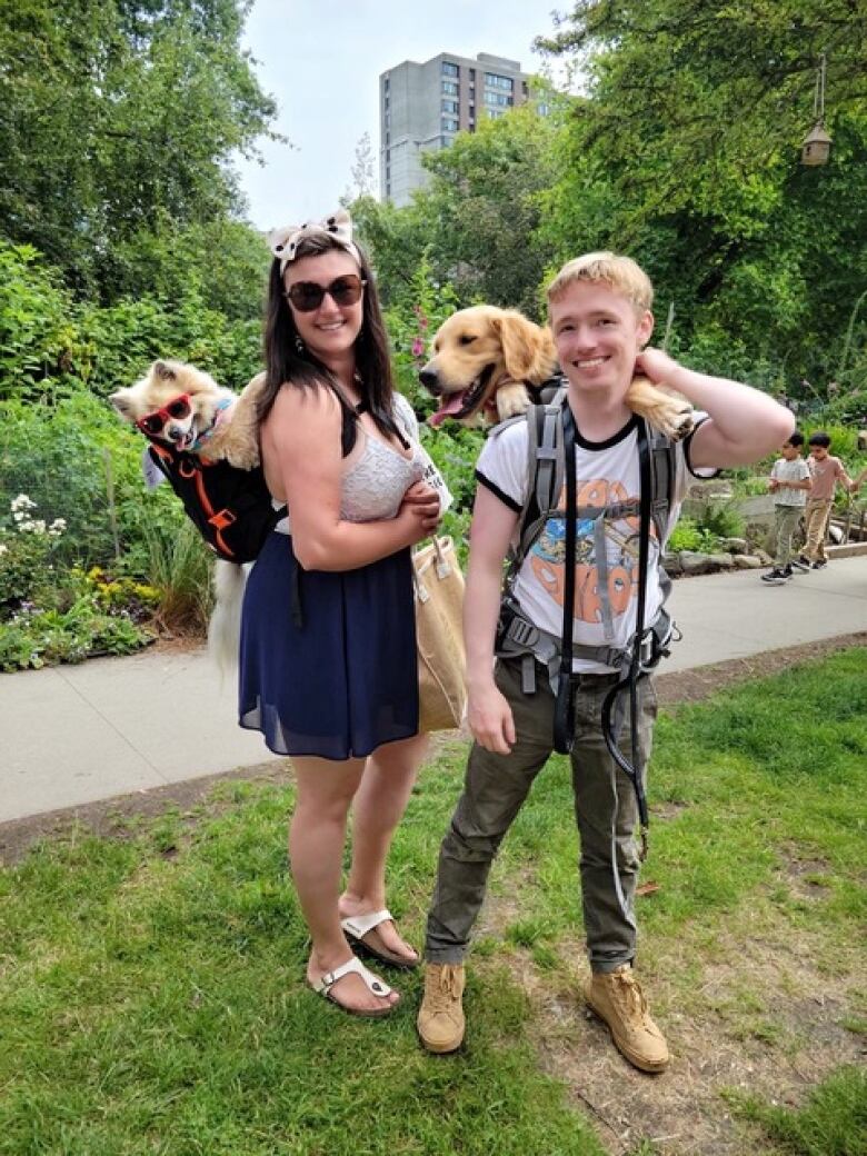 A woman wears a backpack holding a small dog and a man with his large dog in a backpack.