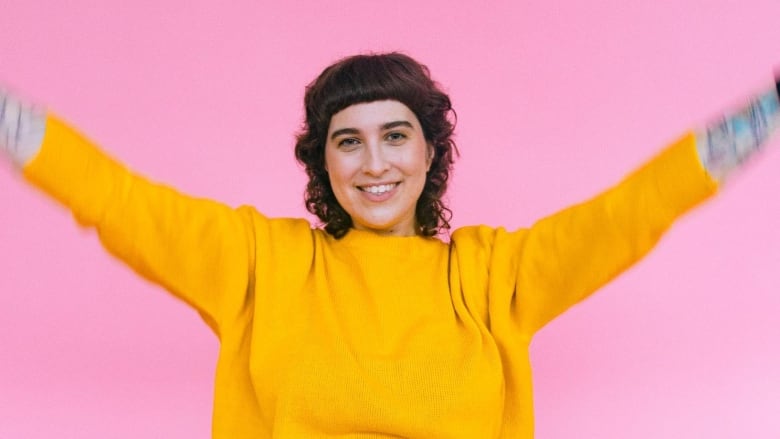 A seated person smiles at the camera with their hands in the air.